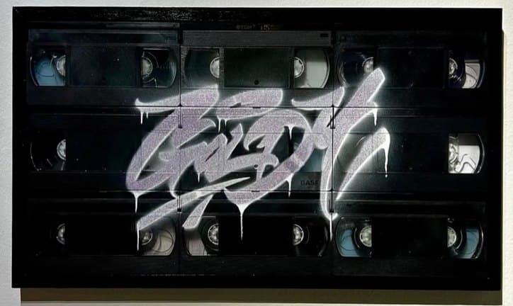 GOLDY Goldi Mikhail Maksimovich A silver-violet Goldy graffiti tag sprayed over a panel of black VHS cassettes.