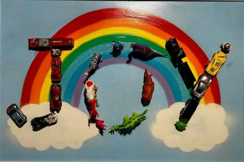 JOY Goldi Mikhail Maksimovich A rainbow over clouds with toy cars and animal figures arranged to spell JOY on plywood.