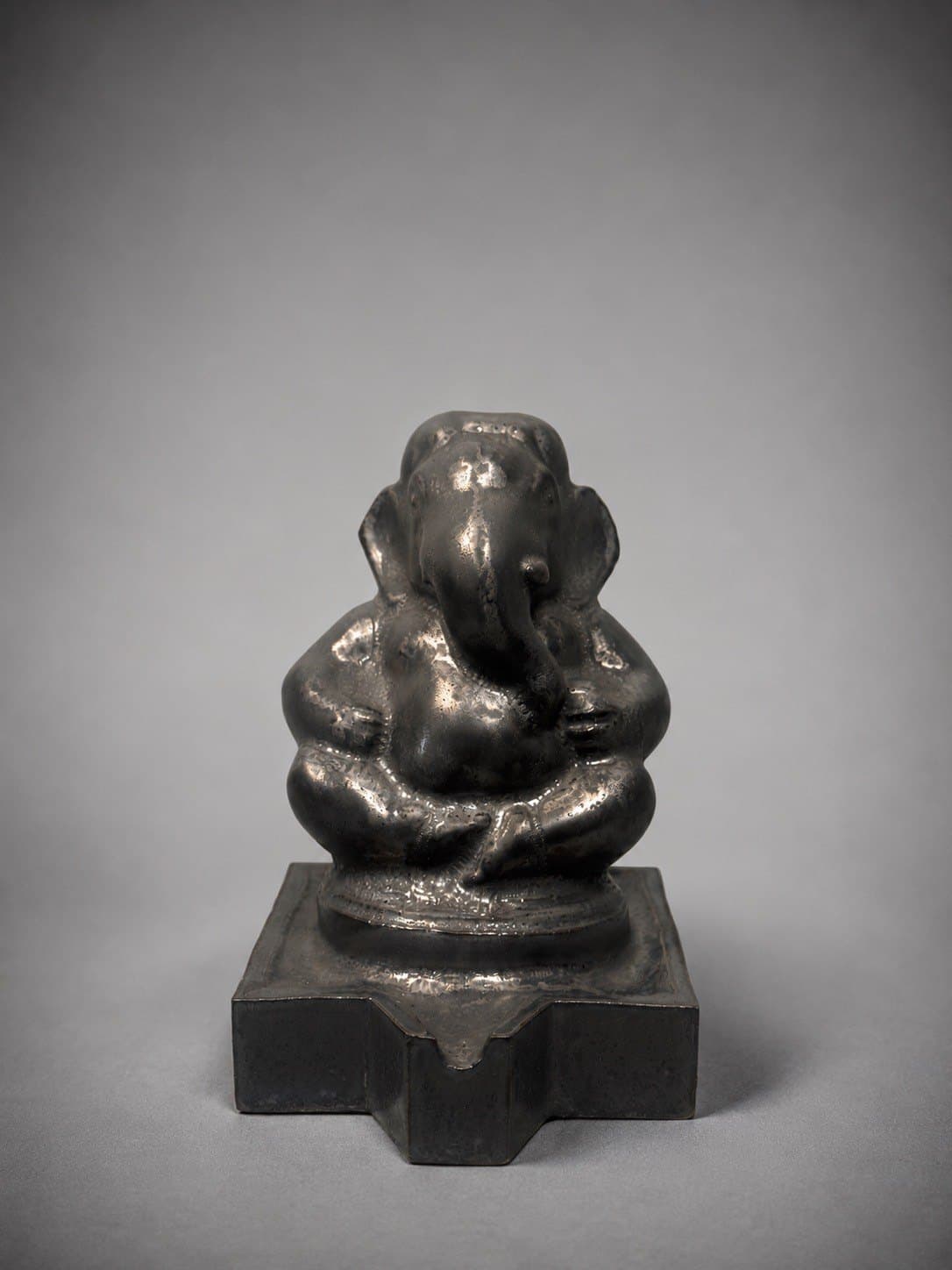 Ganesha – Silver Luster / พระพิฆเนศ เคลือบเงินรมดำ SEO Title (EN): Silver Luster Ganesha – Ceramic by Watcharin Chumek SEO Title (TH): พระพิฆเนศเคลือบเงินรมดำ – เซรามิก วัชรินทร์ ชูเมฆ Meta Description (EN): A seated Ganesha in metallic silver luster glaze with a dark, aged patina, evoking cast metal devotional images. Original ceramic by Thai sculptor Watcharin Chumek. Meta Description (TH): พระพิฆเนศประทับนั่ง เคลือบโลหะสีเงินรมดำ ให้ผิวสัมผัสคล้ายรูปเคารพโลหะเก่า ประติมากรรมเซรามิกต้นฉบับ โดยวัชรินทร์ ชูเมฆ Alt Text (EN): Seated Ganesha sculpture in metallic silver-black luster glaze on a stepped square pedestal with a spout Alt Text (TH): ประติมากรรมพระพิฆเนศประทับนั่ง เคลือบโลหะสีเงินรมดำ บนฐานสี่เหลี่ยมย่อมุมมีรางน้ำ URL slug: watcharin-chumek-ganesha-silver-luster Keywords: silver Ganesha, metallic glaze Ganesha, black Ganesha statue, พระพิฆเนศสีเงิน, พระพิฆเนศรมดำ