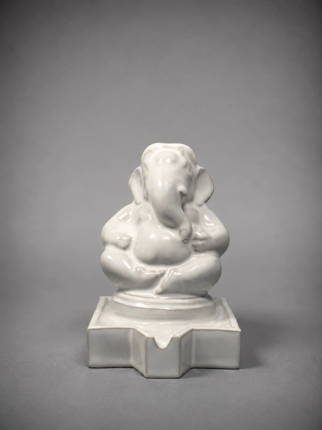 Ganesha – Pure White / พระพิฆเนศ เคลือบขาว SEO Title (EN): White Ganesha – Ceramic Sculpture by Watcharin Chumek SEO Title (TH): พระพิฆเนศเคลือบขาว – ประติมากรรม วัชรินทร์ ชูเมฆ Meta Description (EN): A serene seated Ganesha in soft white glaze, its rounded forms gently catching the light. A minimal devotional ceramic by Thai sculptor Watcharin Chumek. Meta Description (TH): พระพิฆเนศประทับนั่งอย่างสงบ เคลือบสีขาวนวล รูปทรงโค้งมนรับแสงอย่างอ่อนโยน ประติมากรรมรูปเคารพแบบมินิมอล โดยวัชรินทร์ ชูเมฆ Alt Text (EN): Small seated Ganesha ceramic sculpture in white glaze on a stepped square pedestal with a spout Alt Text (TH): ประติมากรรมเซรามิกพระพิฆเนศองค์เล็กประทับนั่ง เคลือบสีขาว บนฐานสี่เหลี่ยมย่อมุมมีรางน้ำ URL slug: watcharin-chumek-ganesha-white Keywords: white Ganesha, minimalist Ganesha statue, พระพิฆเนศสีขาว, พระพิฆเนศมินิมอล