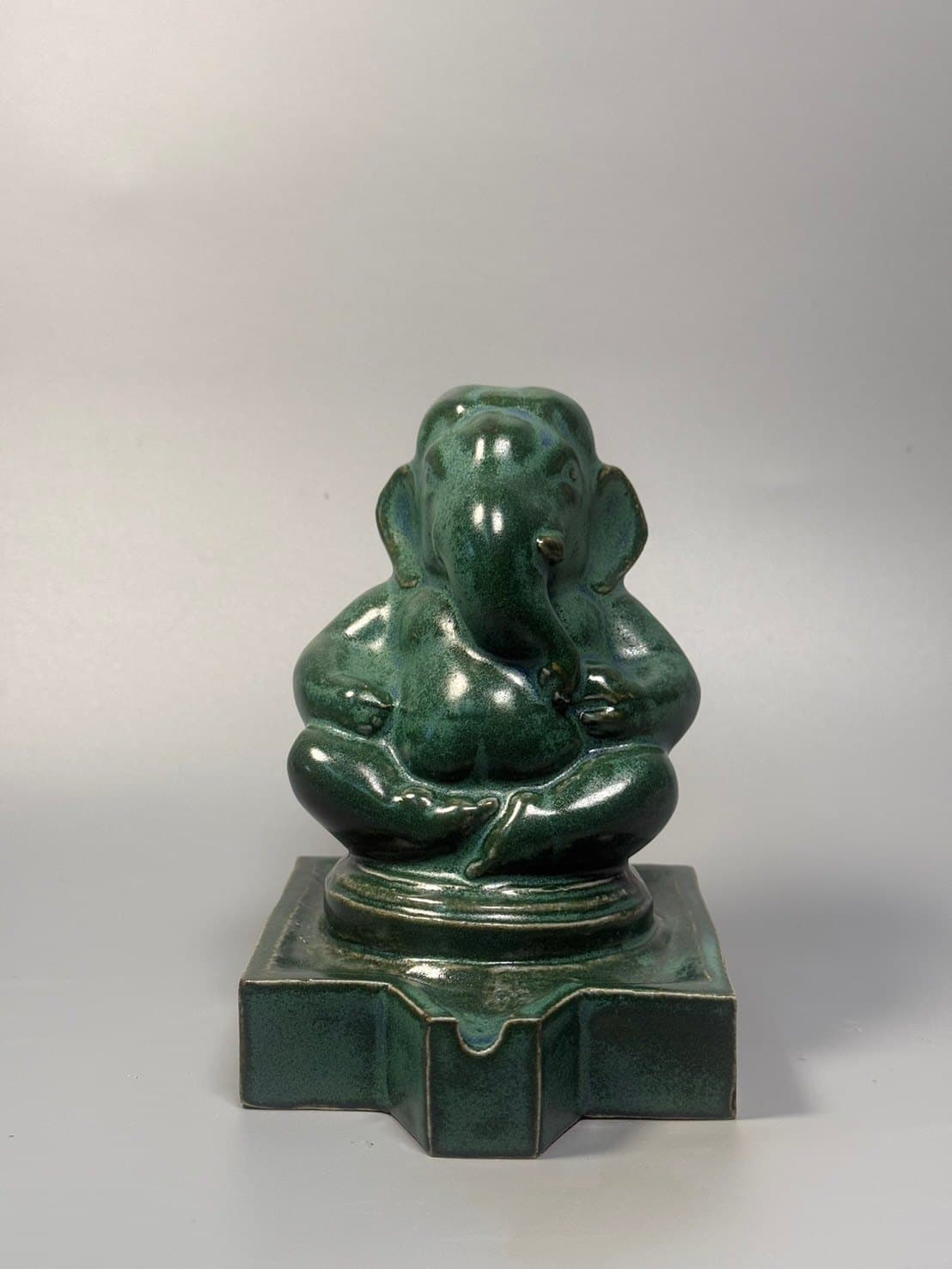 Ganesha – Forest Green / พระพิฆเนศ เคลือบเขียวป่า SEO Title (EN): Forest Green Ganesha – Ceramic by Watcharin Chumek SEO Title (TH): พระพิฆเนศเคลือบเขียวป่า – เซรามิก วัชรินทร์ ชูเมฆ Meta Description (EN): A seated Ganesha in deep forest-green glaze with subtle blue undertones, resting on a stepped pedestal with a water spout. Original ceramic by Thai sculptor Watcharin Chumek. Meta Description (TH): พระพิฆเนศประทับนั่งขัดสมาธิ เคลือบสีเขียวเข้มแซมประกายฟ้า บนฐานย่อมุมพร้อมรางน้ำ ประติมากรรมเซรามิกต้นฉบับ โดยวัชรินทร์ ชูเมฆ Alt Text (EN): Small seated Ganesha ceramic sculpture in dark green glaze on a stepped square pedestal with a spout Alt Text (TH): ประติมากรรมเซรามิกพระพิฆเนศองค์เล็กประทับนั่ง เคลือบสีเขียวเข้ม บนฐานสี่เหลี่ยมย่อมุมมีรางน้ำ URL slug: watcharin-chumek-ganesha-forest-green Keywords: green Ganesha, ceramic Ganesha statue, พระพิฆเนศสีเขียว, พระพิฆเนศเซรามิก
